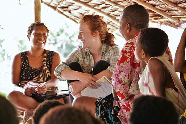 Female student with red hair smiles warmly with in an international setting with native students and adults. 