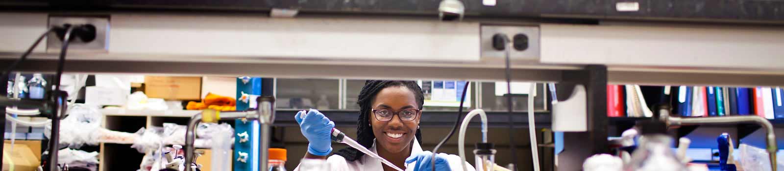 A graduate student holding a pipette and smiling in a laboratory